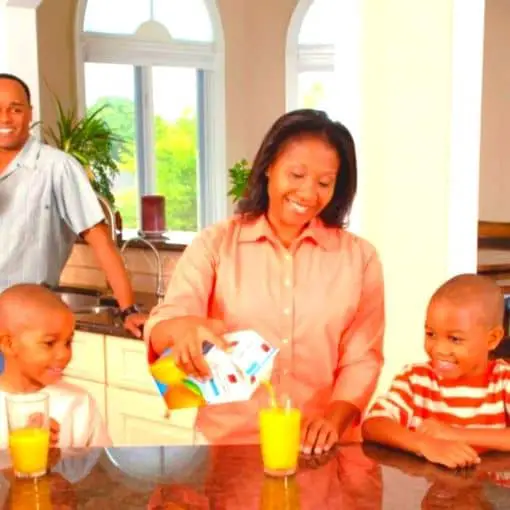 Photo of a family, mother pouring orange juice for sons as a father looks on representing sibling DNA.