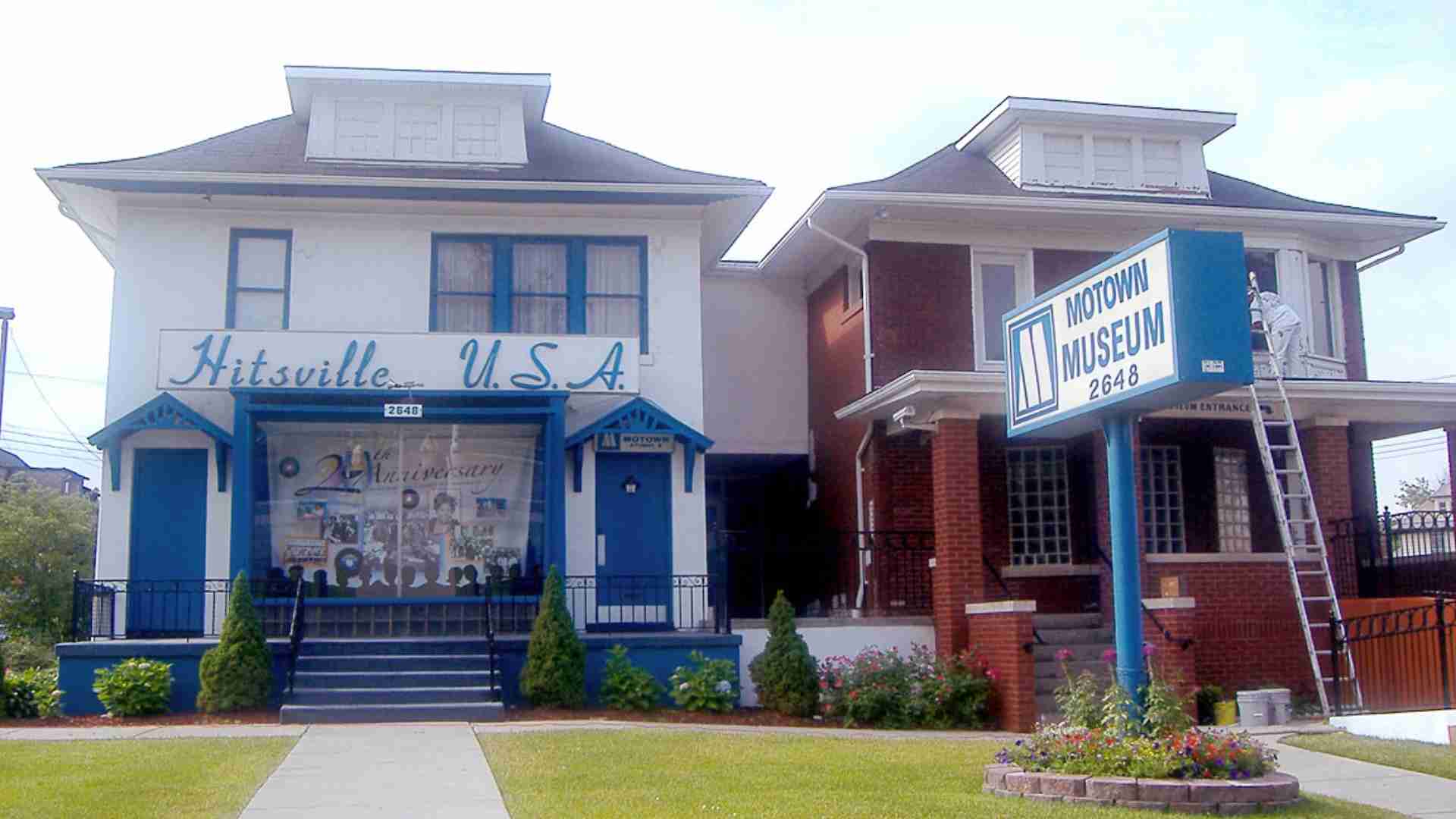 Two neighboring museum buildings: Hitsville U.S.A. on the left and Motown Museum on the right, with blue trim and a large sign on the corner.